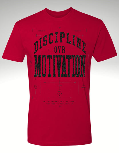 A red short-sleeve crewneck t-shirt with a distressed black graphic print on the front reading 'DISCIPLINE OVR MOTIVATION' over a blueprint-style background.